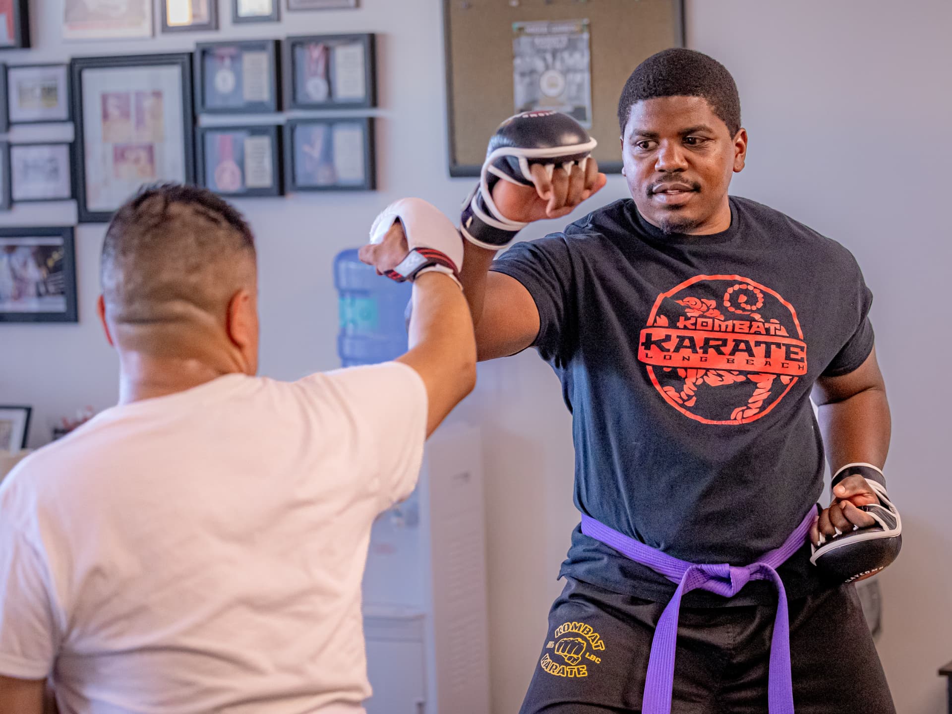 Instructor holding pads for a teen and adult karate student during striking practice at Kombat Karate Long Beach