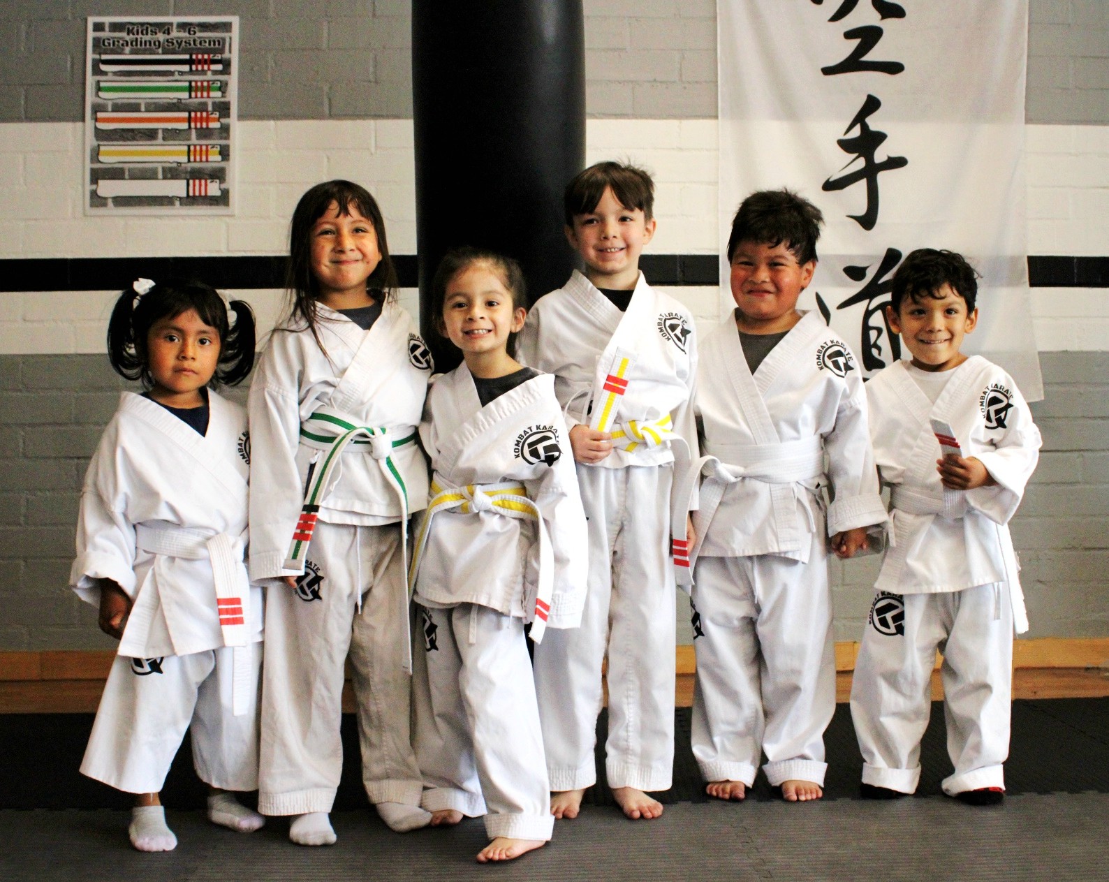 Group of young karate students in white gis smiling at Kombat Karate in Long Beach, CA